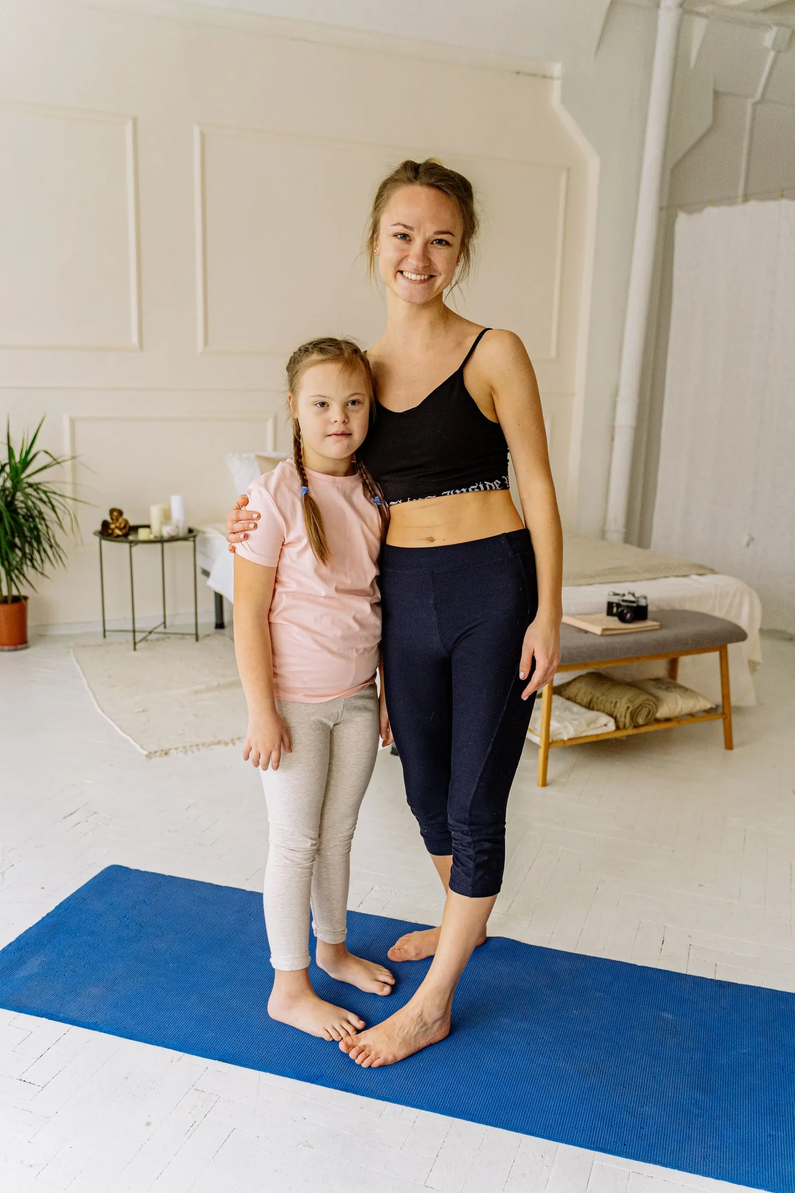 Smiling therapist and young girl standing together on an exercise mat